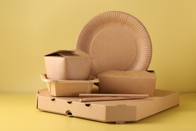 Photo of Eco friendly food packaging. Paper containers and tableware on pale yellow background