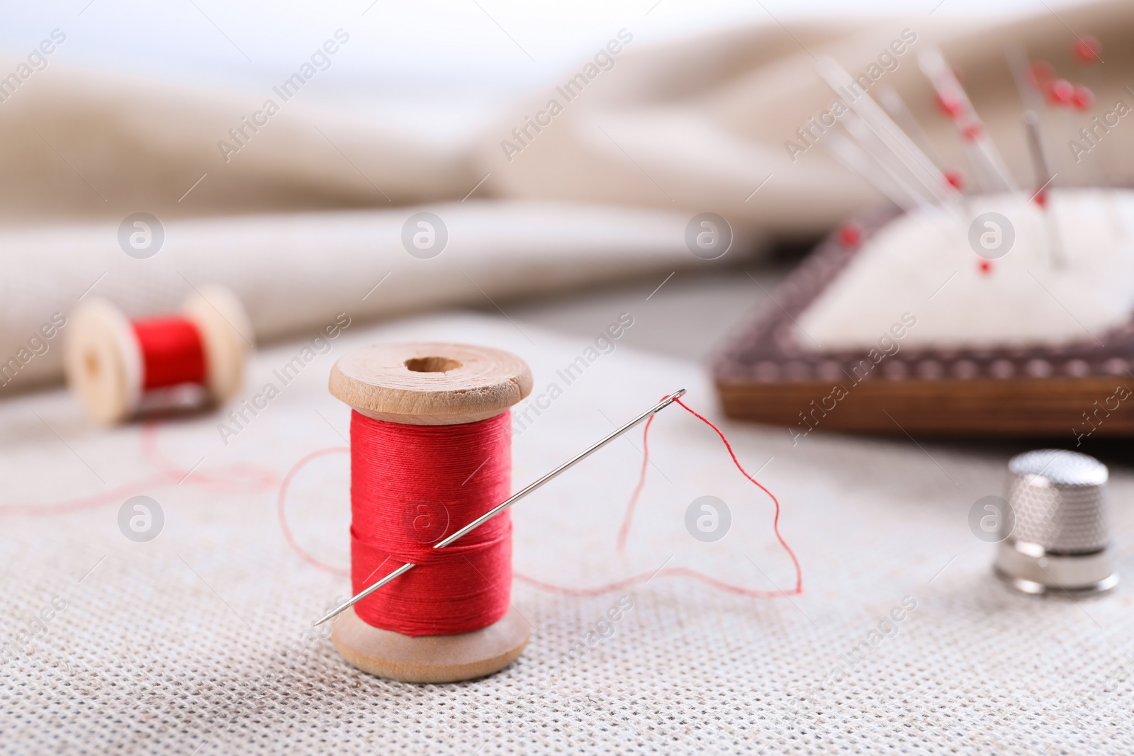 Photo of Spool of red sewing thread with needle on white fabric