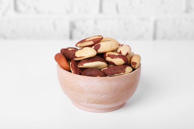 Bowl with tasty Brazil nuts on white table against brick wall