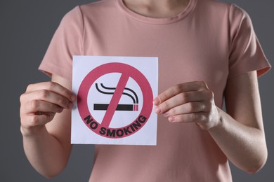 Photo of Woman holding card with no smoking sign on gray background, closeup