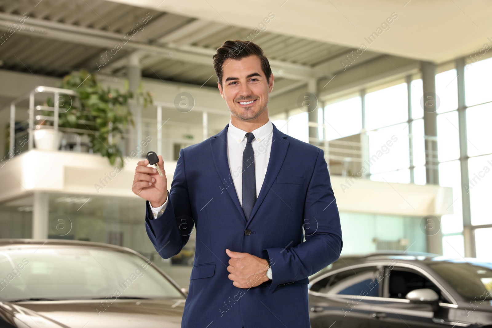 Photo of Young salesman with car key in modern dealership