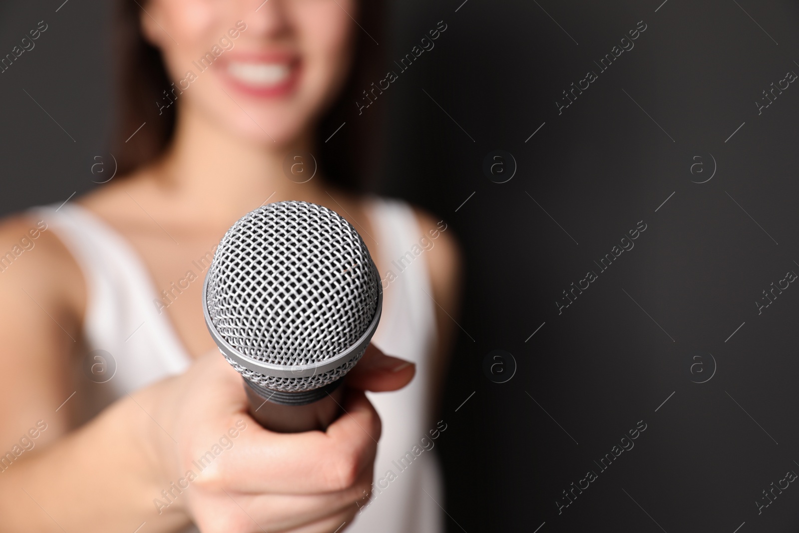 Photo of Young woman holding microphone on dark background, closeup view with space for text