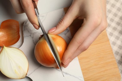 Photo of Woman cutting ripe onion at white table, top view