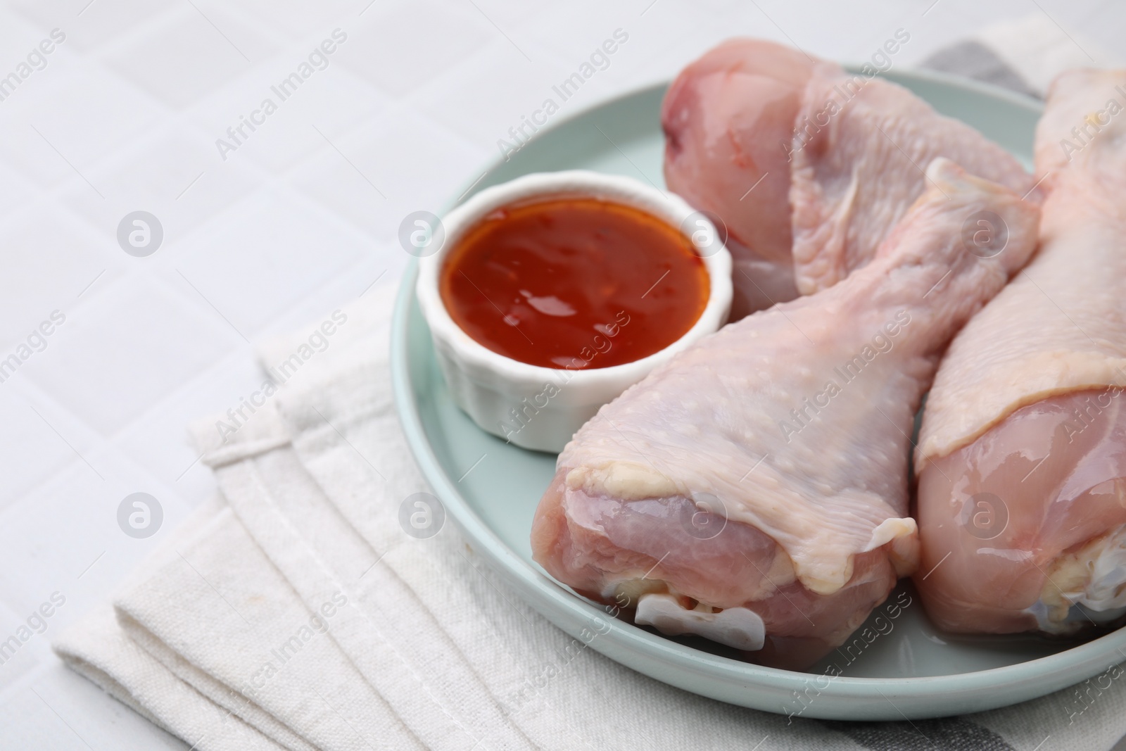 Photo of Fresh marinade and raw chicken drumsticks on white tiled table, closeup. Space for text