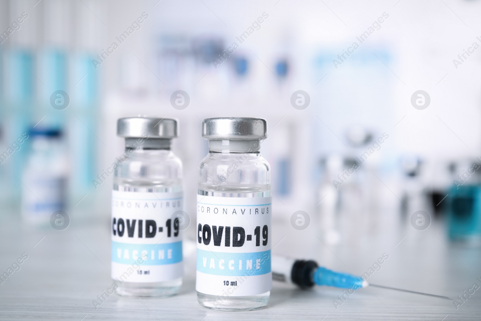 Photo of Vials with vaccine against Covid-19 and syringe on white table indoors