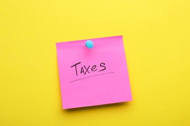 Photo of Paper note with word Taxes pinned on yellow background