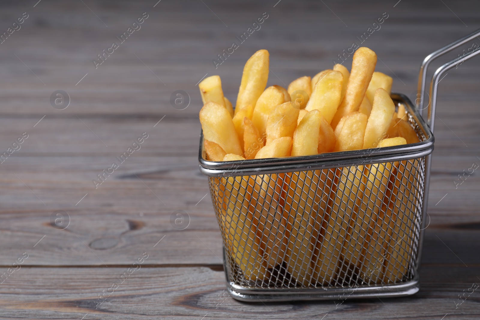 Photo of Metal basket with tasty French fries on grey wooden table, closeup. Space for text