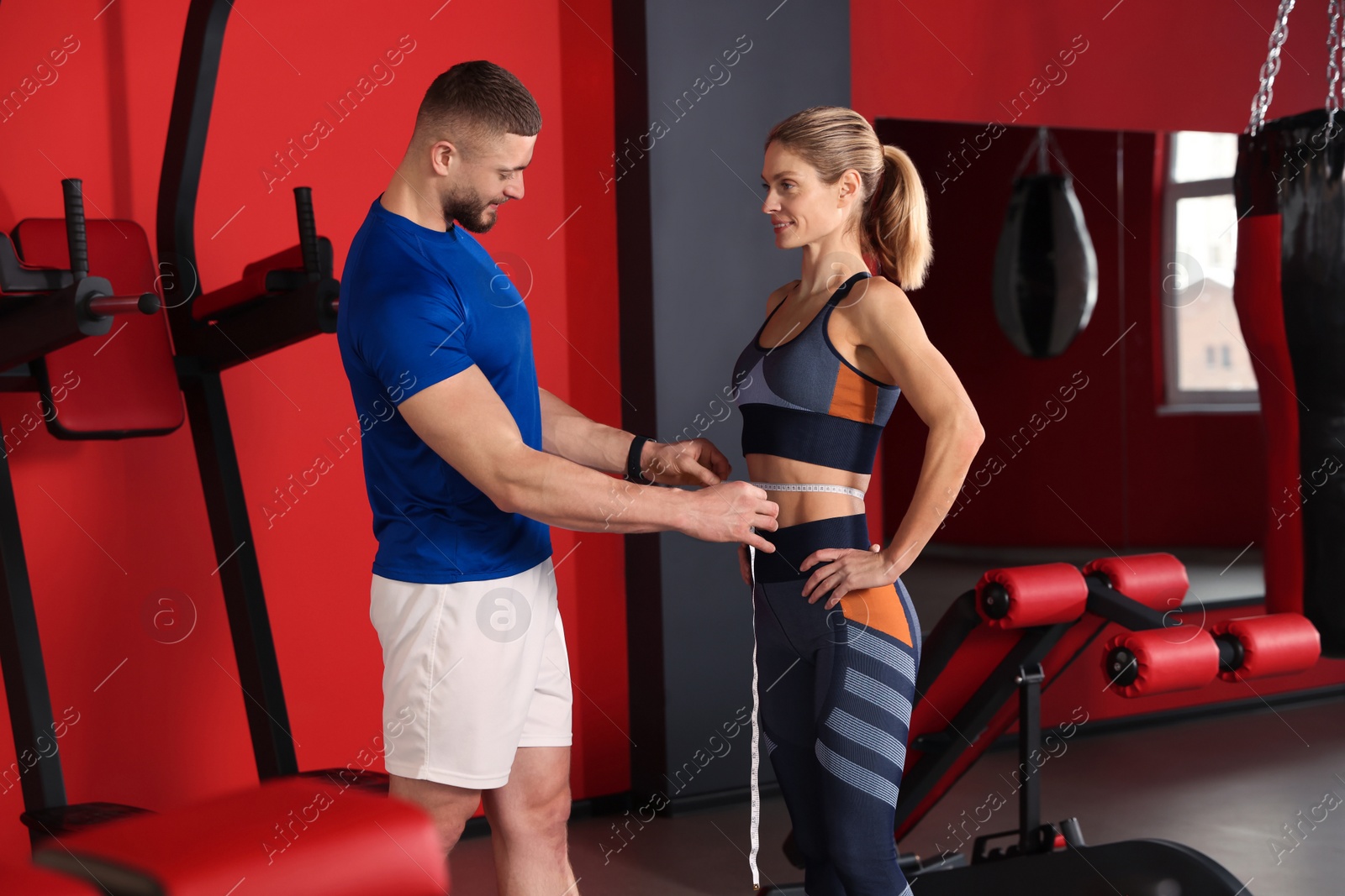 Photo of Trainer measuring woman`s waist with tape in gym