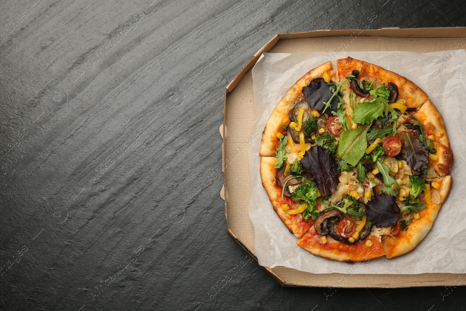 Photo of Delicious vegetarian pizza with mushrooms, vegetables and greens in box on black table, top view. Space for text