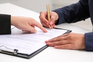 Businesswoman showing client where to sign document at white table, closeup