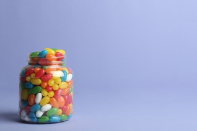 Photo of Glass jar with delicious bright jelly beans on color background. Space for text