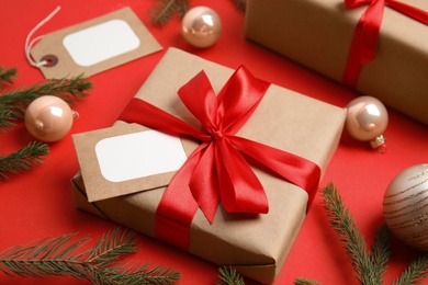 Photo of Gift box with blank tag and Christmas decor on red background, closeup