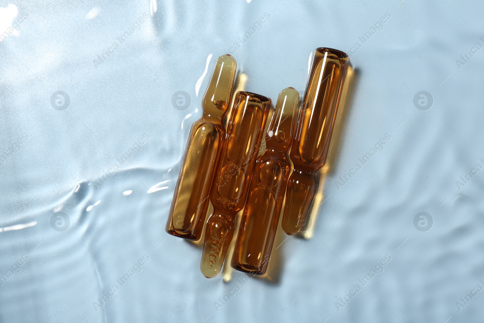 Photo of Skincare ampoules in water on light blue background, top view