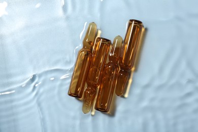 Skincare ampoules in water on light blue background, top view