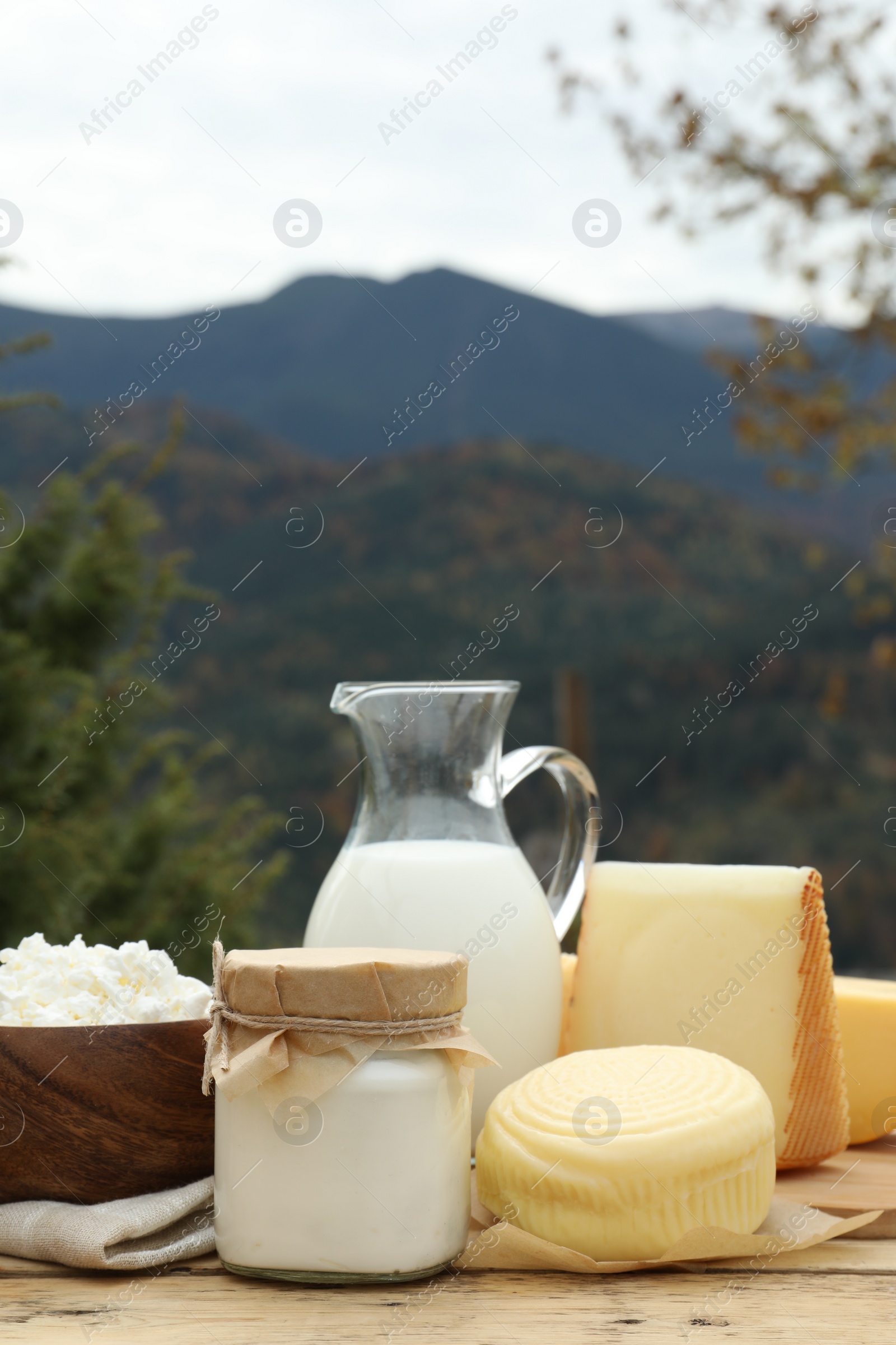 Photo of Tasty cottage cheese and other fresh dairy products on wooden table in mountains