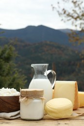 Photo of Tasty cottage cheese and other fresh dairy products on wooden table in mountains