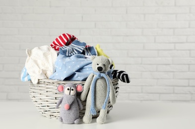 Photo of Wicker basket with laundry and toys on table near white brick wall. Space for text