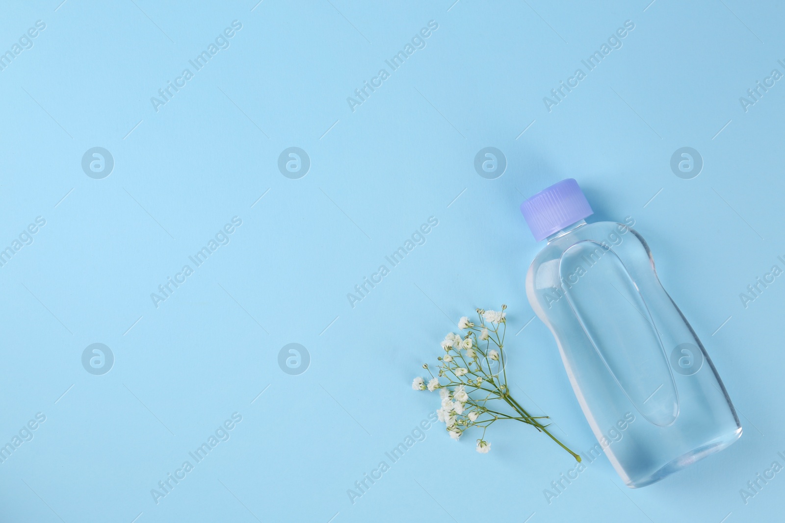 Photo of Bottle with baby oil and gypsophila on light blue background, flat lay. Space for text