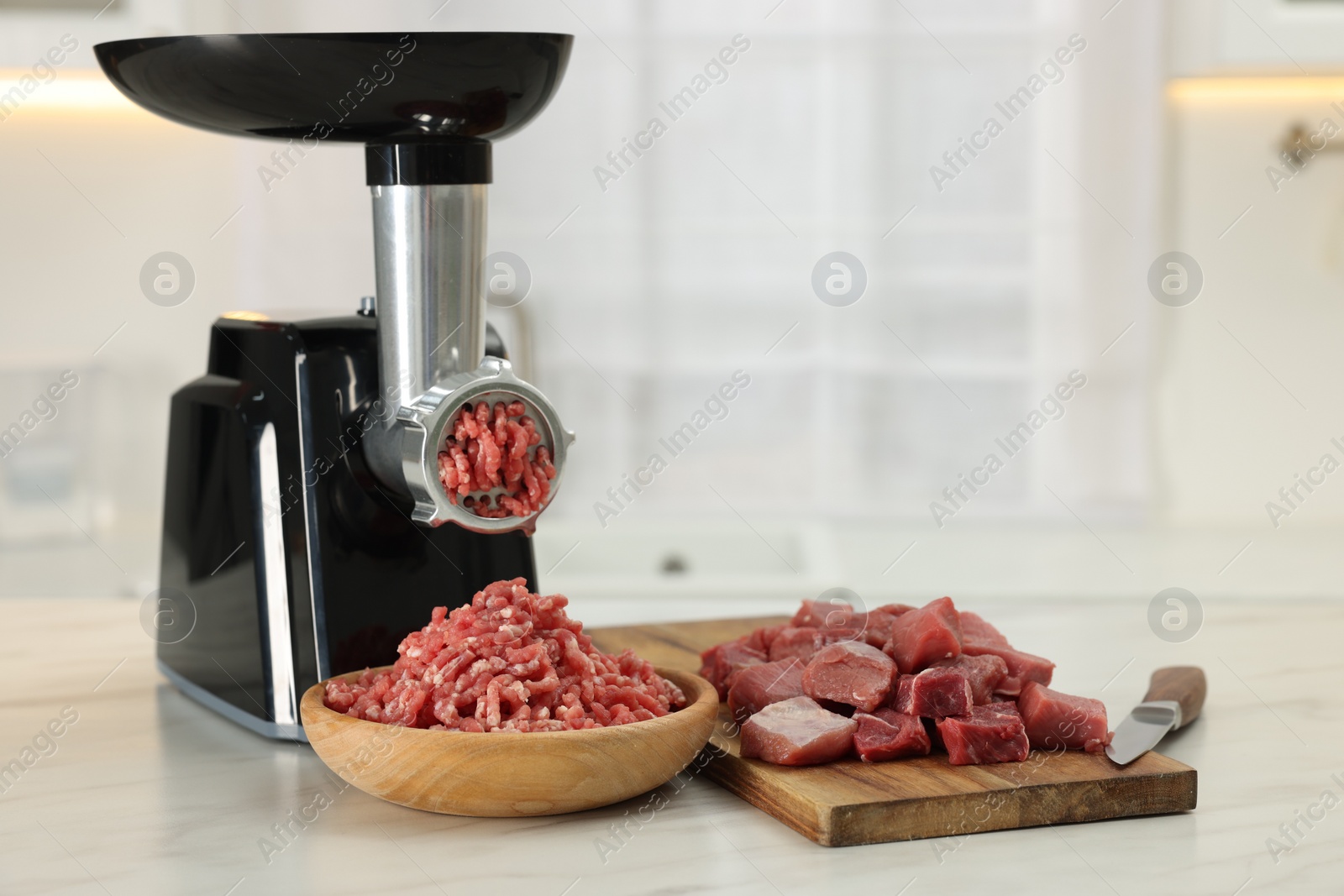 Photo of Electric meat grinder with beef on white marble table in kitchen