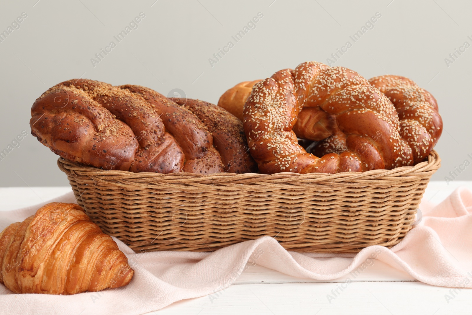 Photo of Wicker basket with different tasty freshly baked pastries on white wooden table