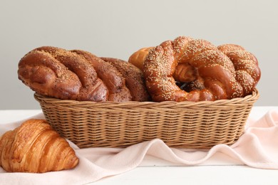 Wicker basket with different tasty freshly baked pastries on white wooden table