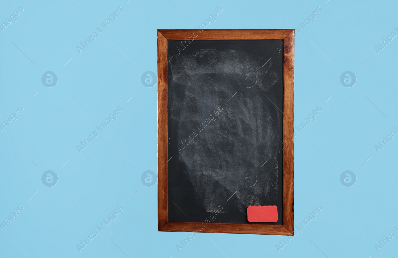 Photo of Dirty black chalkboard with duster on light blue background