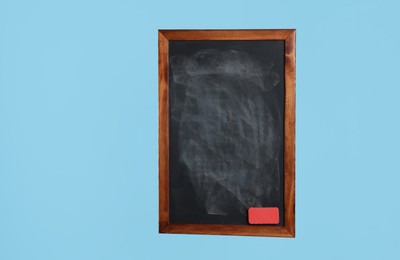 Photo of Dirty black chalkboard with duster on light blue background