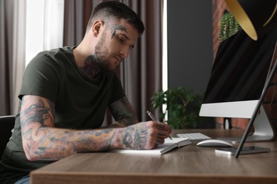Photo of Hipster man writing near computer at wooden table in room