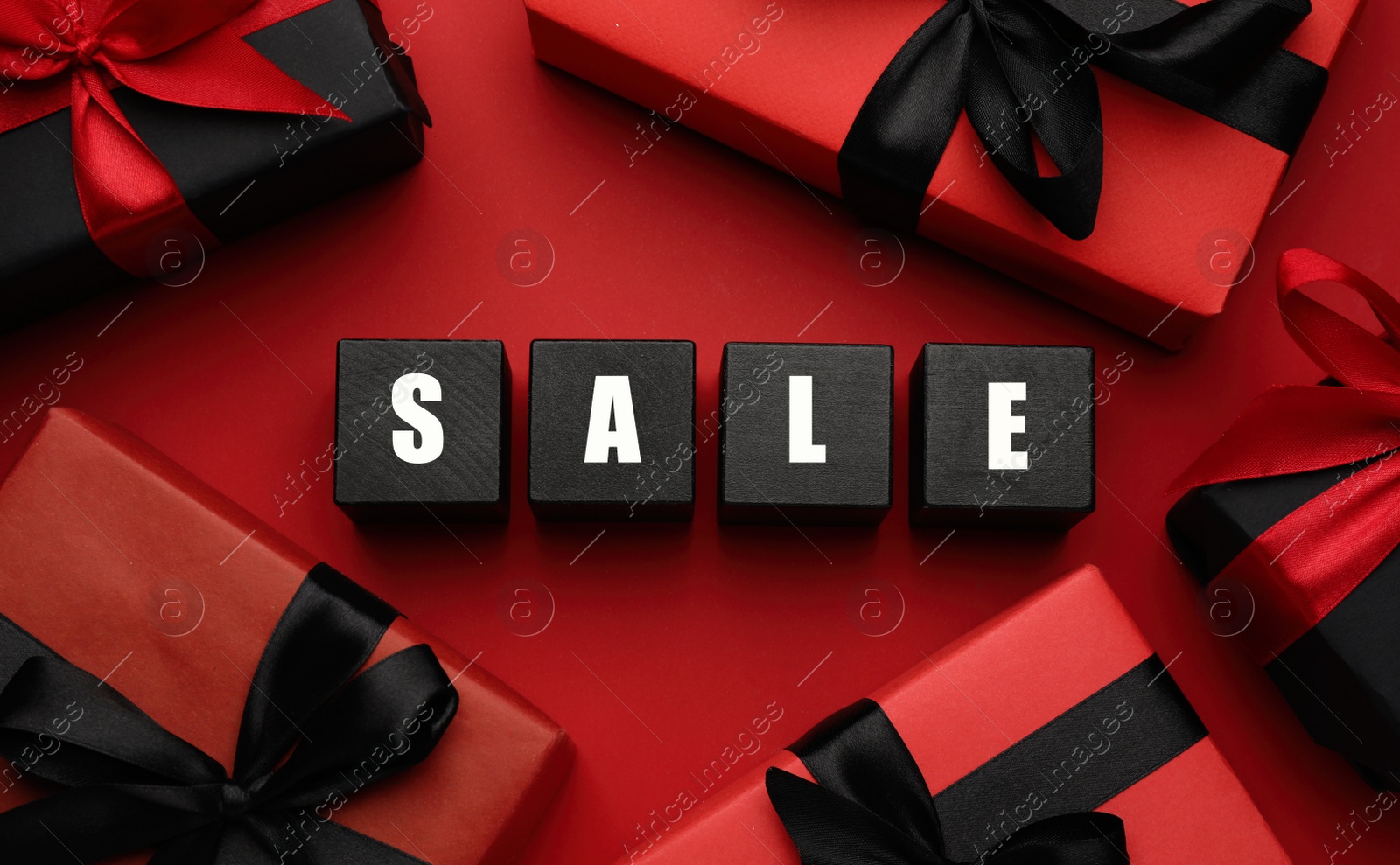 Photo of Wooden cubes with word Sale and gift boxes on red background, flat lay