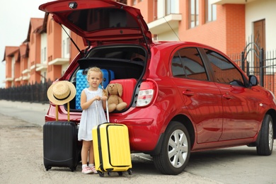Little girl near car trunk with suitcases outdoors