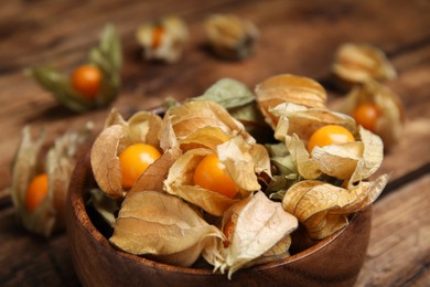 Ripe physalis fruits with dry husk on wooden table, closeup