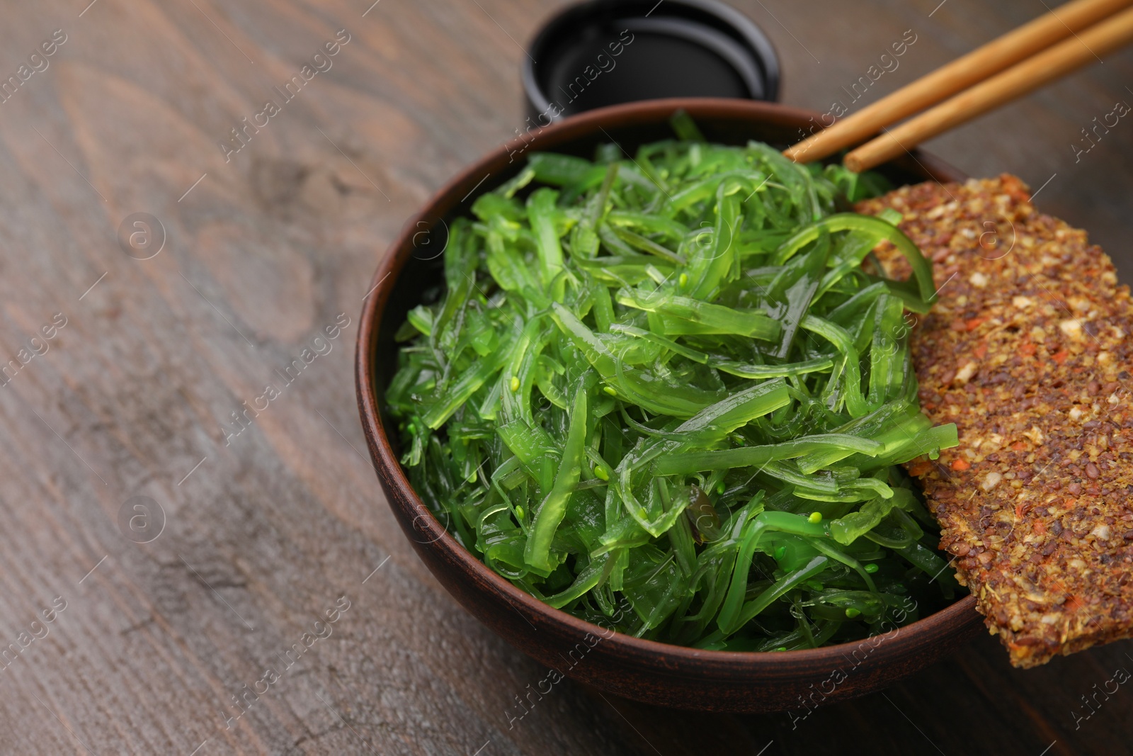 Photo of Tasty seaweed salad in bowl served on wooden table, closeup