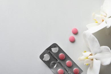 Photo of Pills and orchid flowers on white table, flat lay with space for text. Menopause concept
