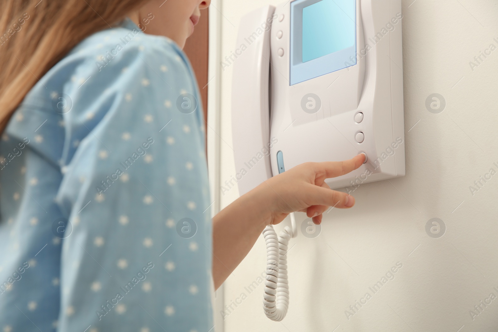 Photo of Cute little girl pressing button on intercom panel indoors, closeup