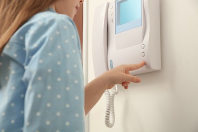 Photo of Cute little girl pressing button on intercom panel indoors, closeup