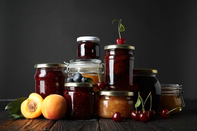 Photo of Jars with different jams and fresh fruits on black wooden table