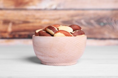 Bowl with tasty Brazil nuts on white wooden table, closeup
