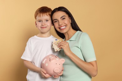 Photo of Mother and her son with ceramic piggy bank on beige background