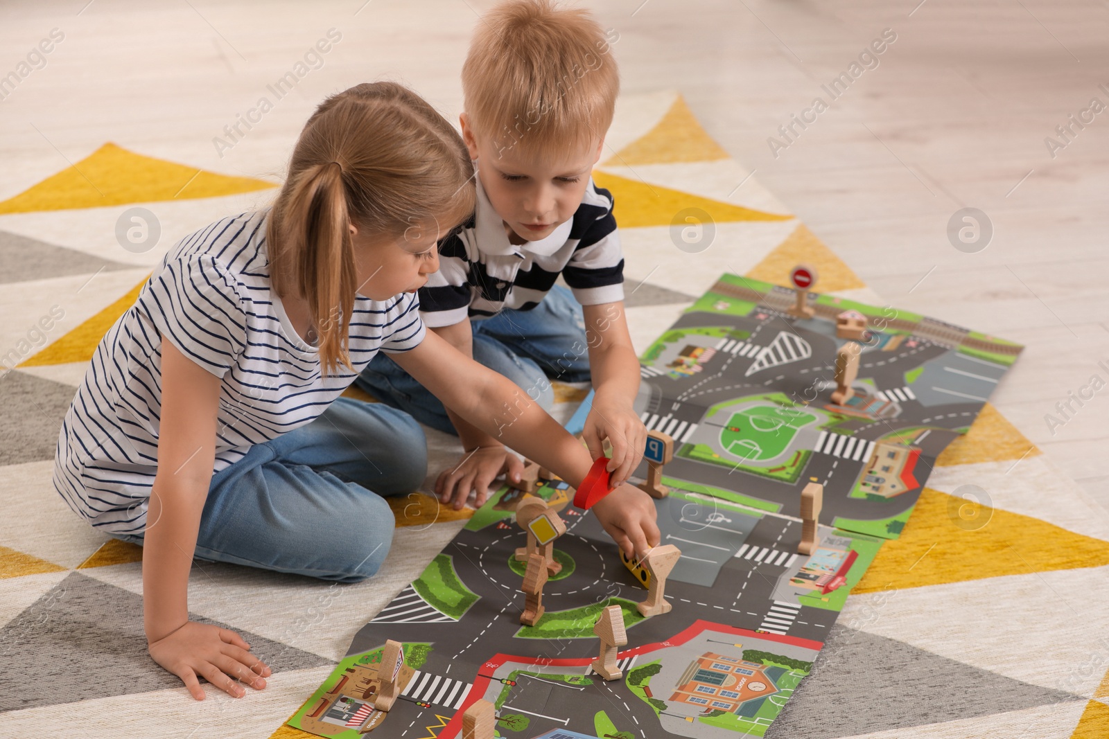 Photo of Little children playing with set of wooden road signs and toy cars indoors