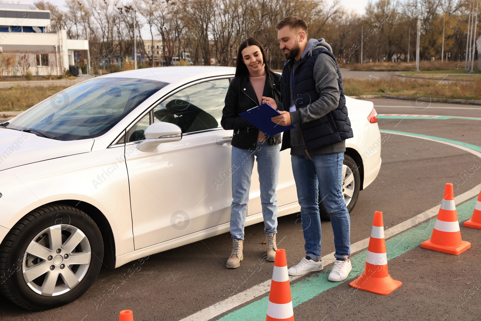 Photo of Young woman with instructor near car at driving school test track