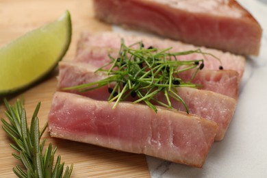 Photo of Pieces of delicious tuna steak with microgreens and rosemary on board, closeup