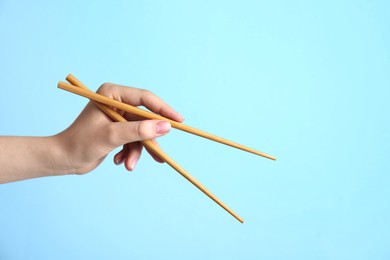 Photo of Woman holding pair of wooden chopsticks on light blue background, closeup