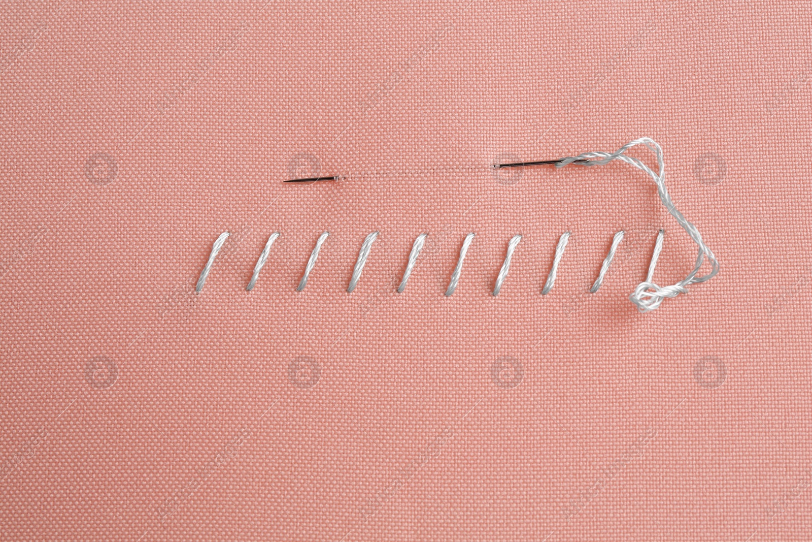 Photo of Sewing needle with thread and stitches on coral cloth, top view