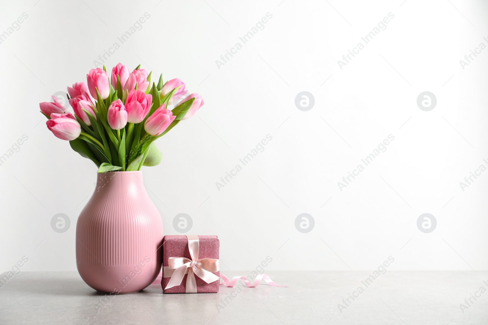 Photo of Bouquet of beautiful spring tulips in vase and gift box on table against white background. International Women's Day