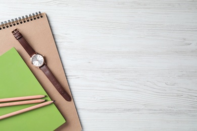 Photo of Notebooks, pencils and wristwatch on white wooden background, top view. Space for text