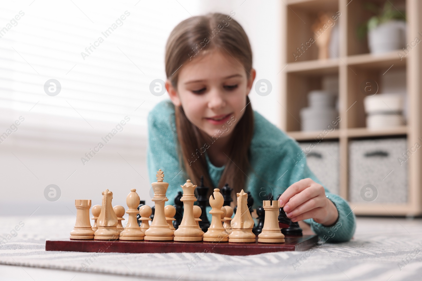 Photo of Cute girl playing chess on floor in room, selective focus