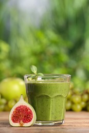 Photo of Glass of fresh green smoothie and ingredients on wooden table outdoors, space for text