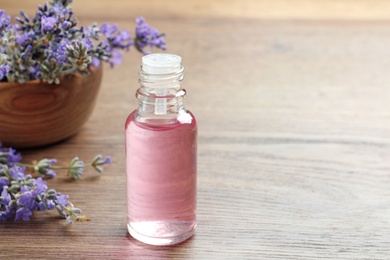 Photo of Bottle of essential oil and lavender flowers on wooden table. Space for text