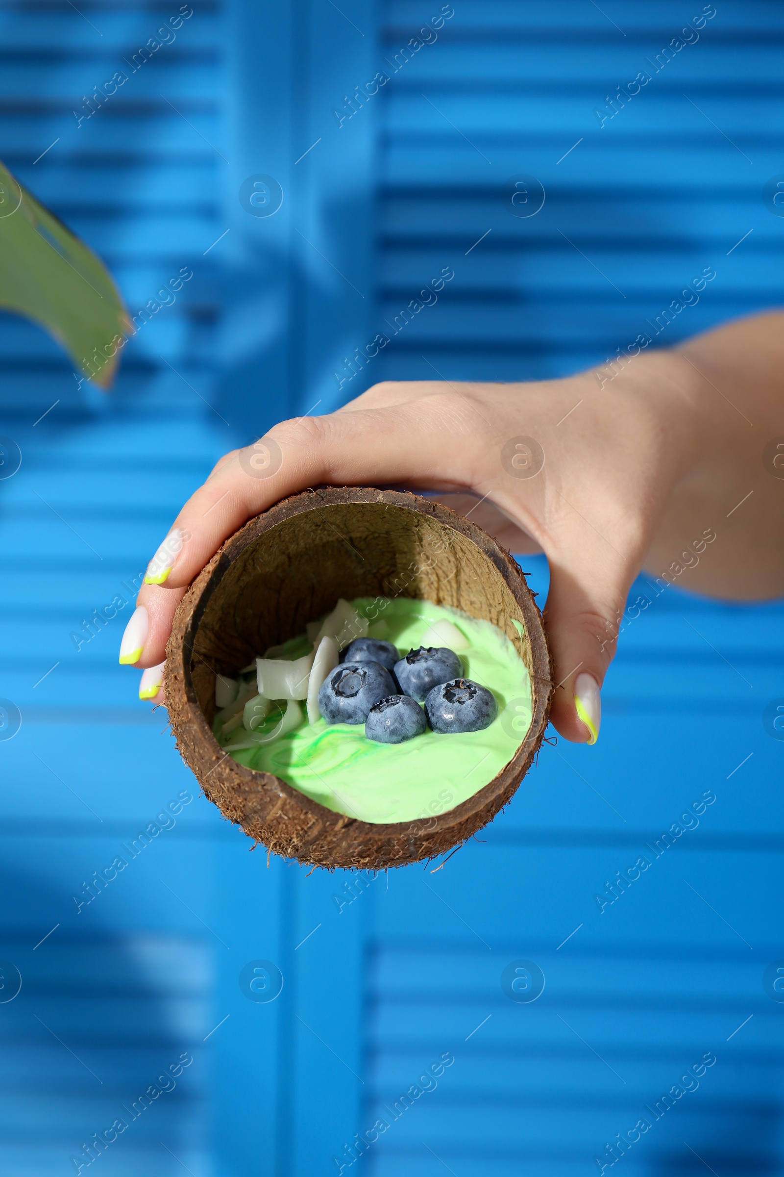 Photo of Woman holding coconut shell with tasty smoothie bowl on blurred background, closeup