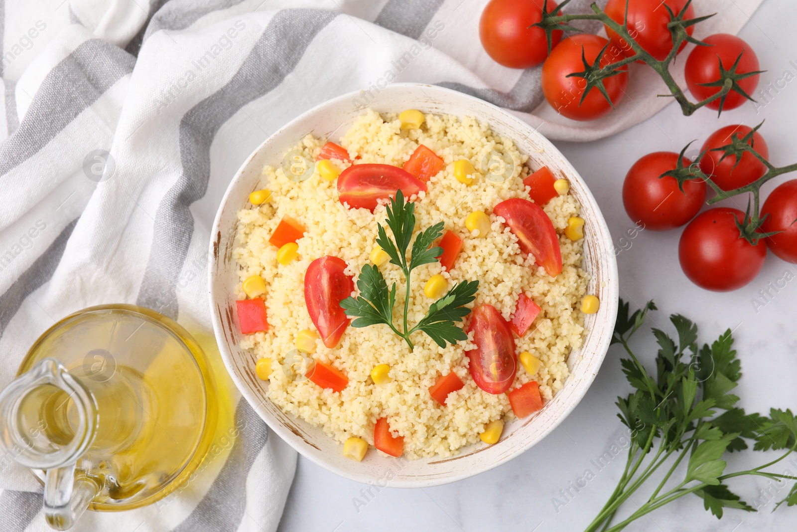 Photo of Tasty couscous with parsley, corn and tomatoes served on white table, flat lay